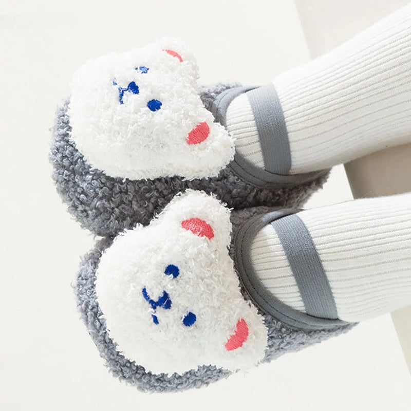 Pair of adorable cartoon bear baby booties with white fur and blue and pink accents on a gray sole.