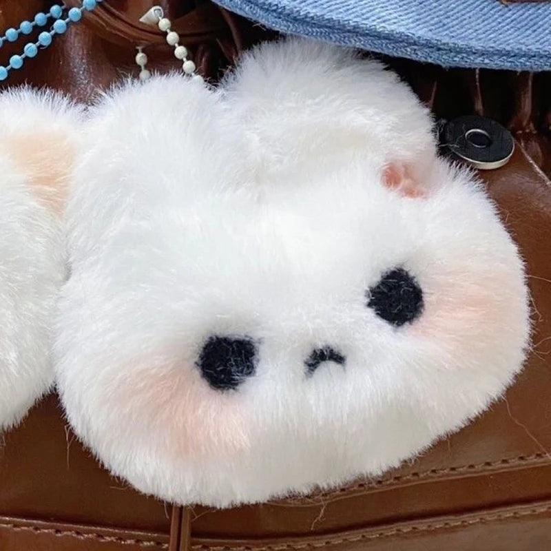 A fluffy white plush rabbit charm with black facial markings resting on brown leather.