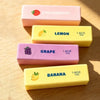 Four squishy fidget toys in pink, yellow, and purple colors labeled strawberry, lemon, grape, and banana