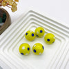 Perles de verre jaunes avec des points bleus arrangées dans un plat blanc carré.