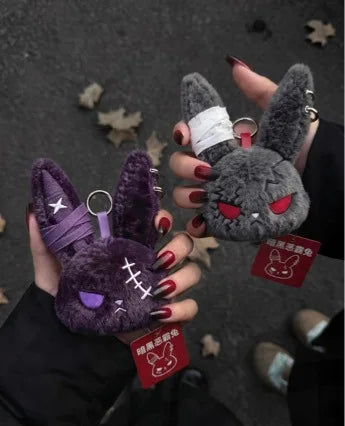 A hand holds a dark purple gothic bunny plush keychain with a white bandage design against a gray background.