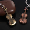 A vintage violin-shaped keychain with gold and copper tones is displayed next to a brown box.
