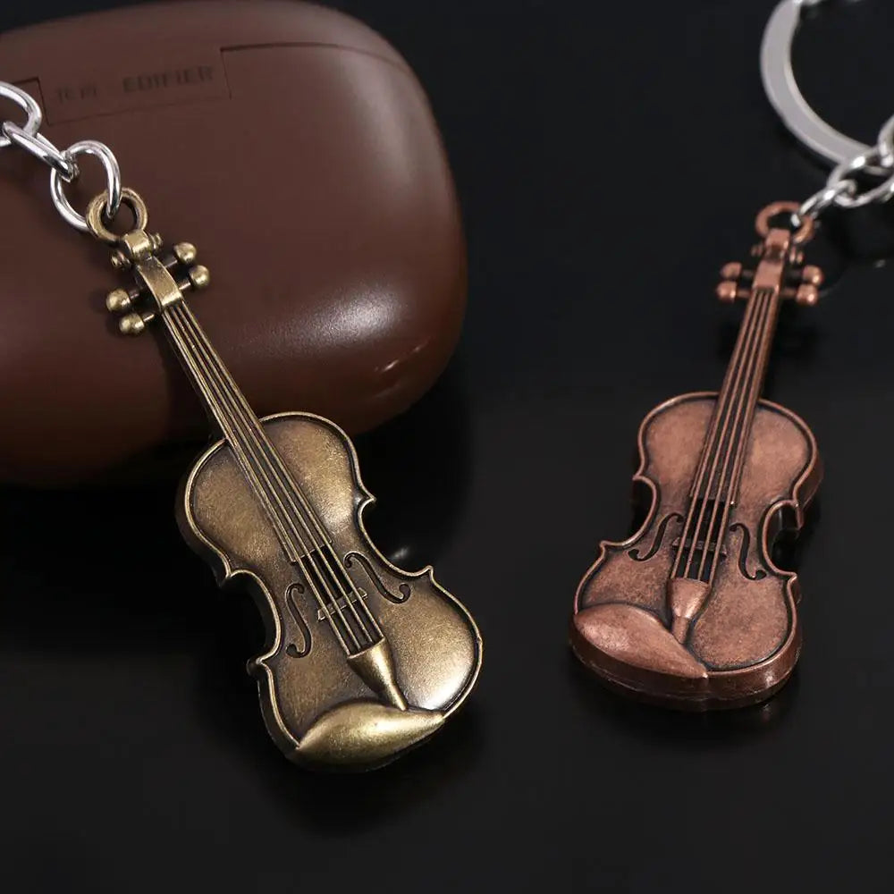 A vintage violin-shaped keychain with gold and copper tones is displayed next to a brown box.