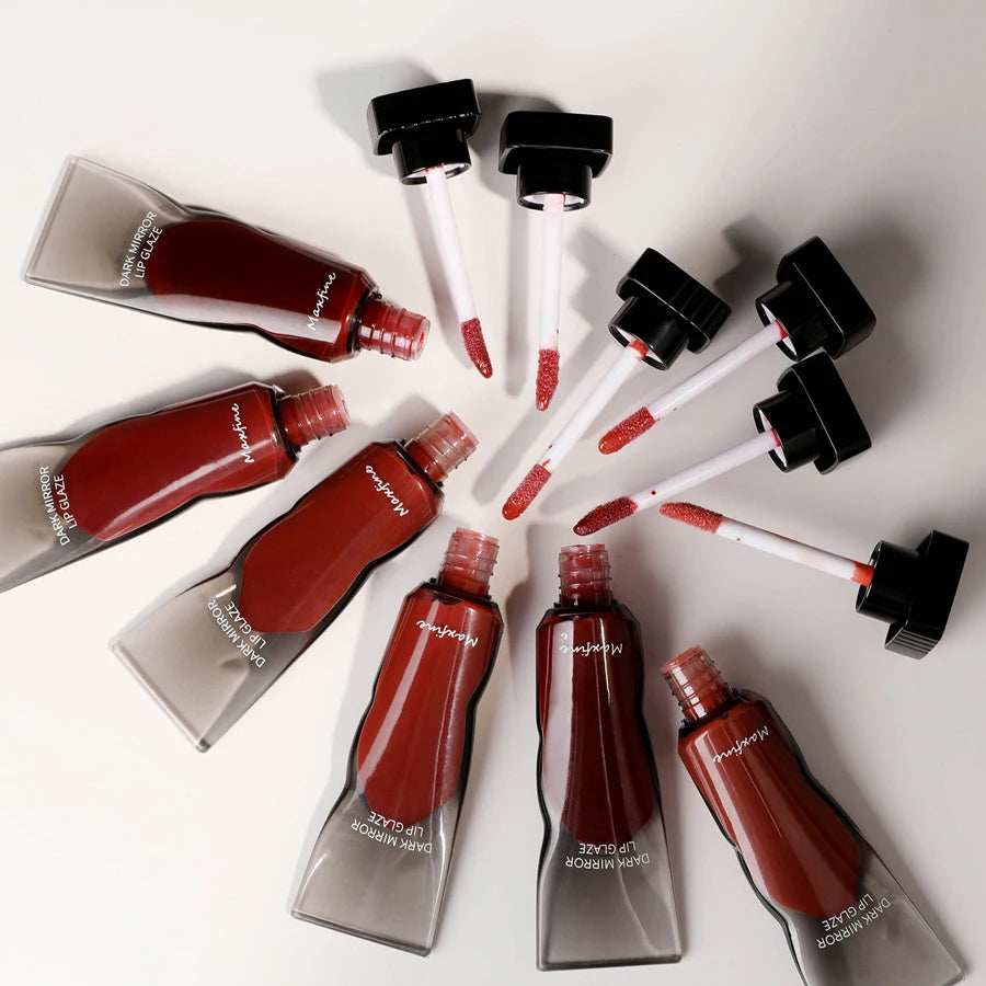 Various bottles of Hydrating Mirror Lip Glaze in dark red and brown shades are displayed on a white surface.