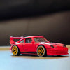 Modelo de coche deportivo rojo a escala 1/64 con ruedas y neumáticos amarillos sobre una superficie clara.