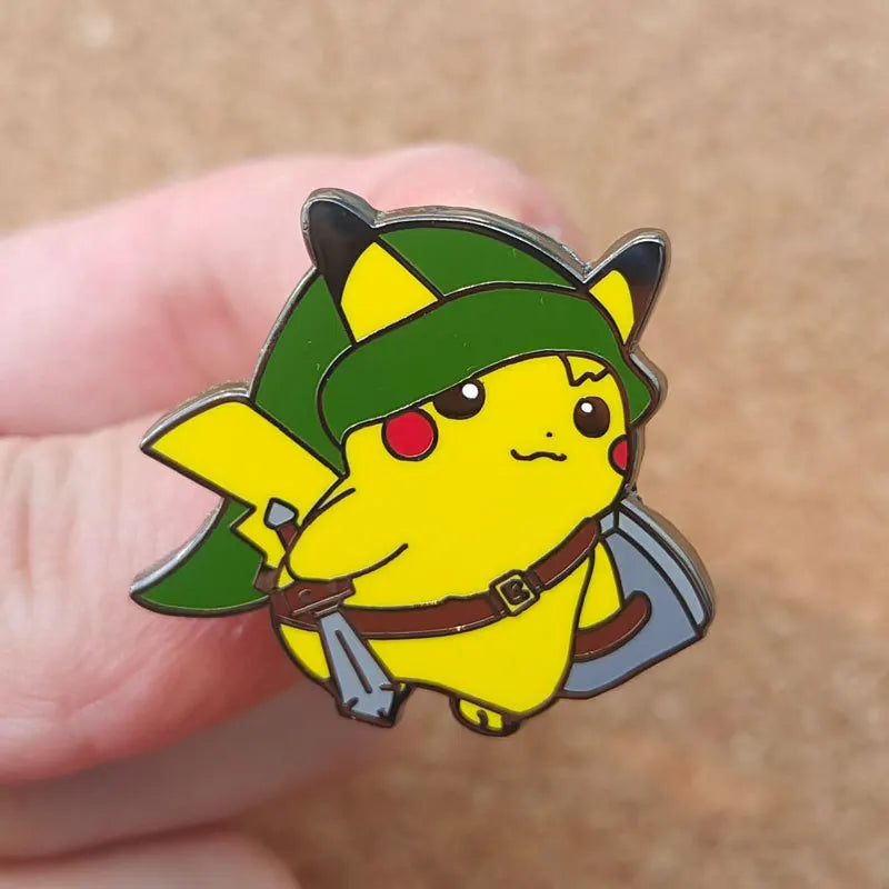 A yellow Pokémon enamel pin featuring a green hat and a brown belt, held by a person's finger.