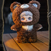 A brown bear plush doll with white hair and blue eyes wearing a hood, sitting on a wooden surface.