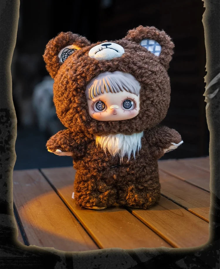 A brown bear plush doll with white hair and blue eyes wearing a hood, sitting on a wooden surface.