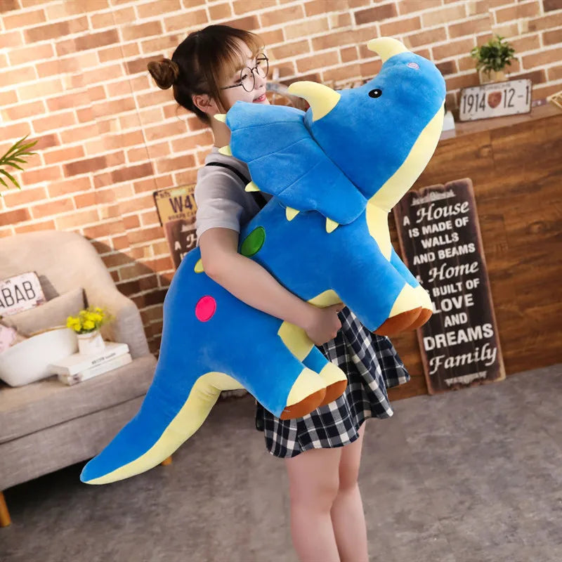 A young girl is holding a large blue dinosaur plush toy in a brick-walled room.