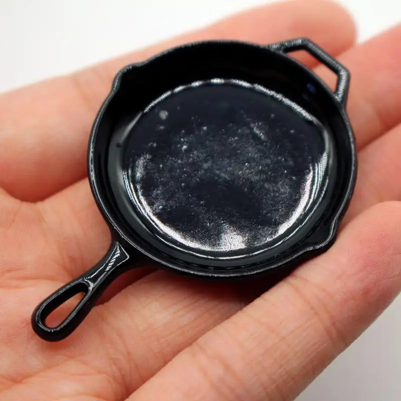 A small, black miniature copper soup pot with handles is held in a person's hand.