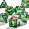 A collection of green polyhedral dice with a gold galaxy finish are displayed on a white surface.