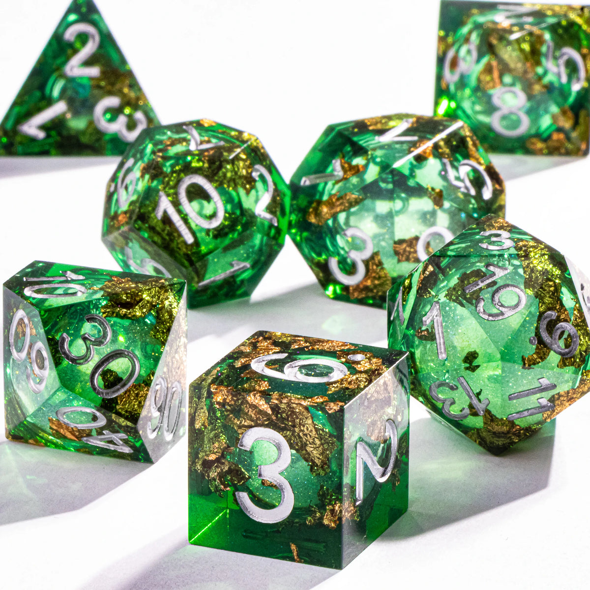 A collection of green polyhedral dice with a gold galaxy finish are displayed on a white surface.