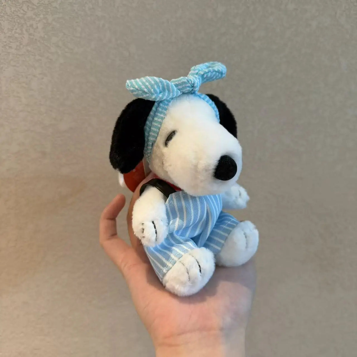 A white Snoopy plush toy with blue striped clothing and a blue bow is held in a hand.