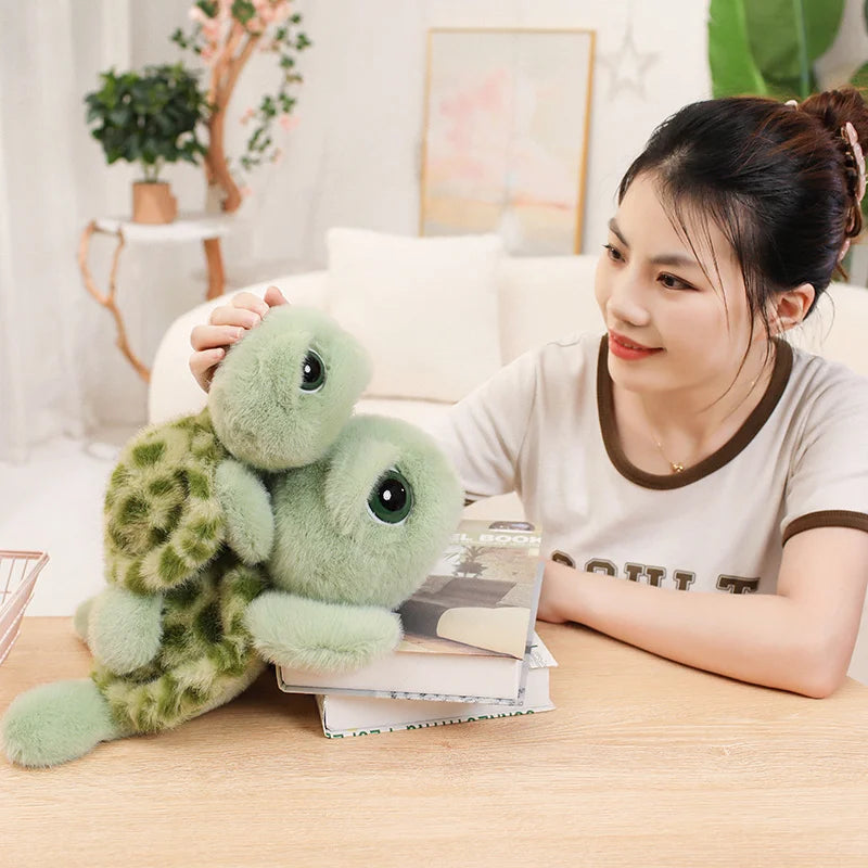 A young woman is holding a soft green sea turtle plush toy on a wooden table.