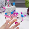A hand holds a pink balloon model made from a clear bubble, next to other colorful balloons and an inflator tool.