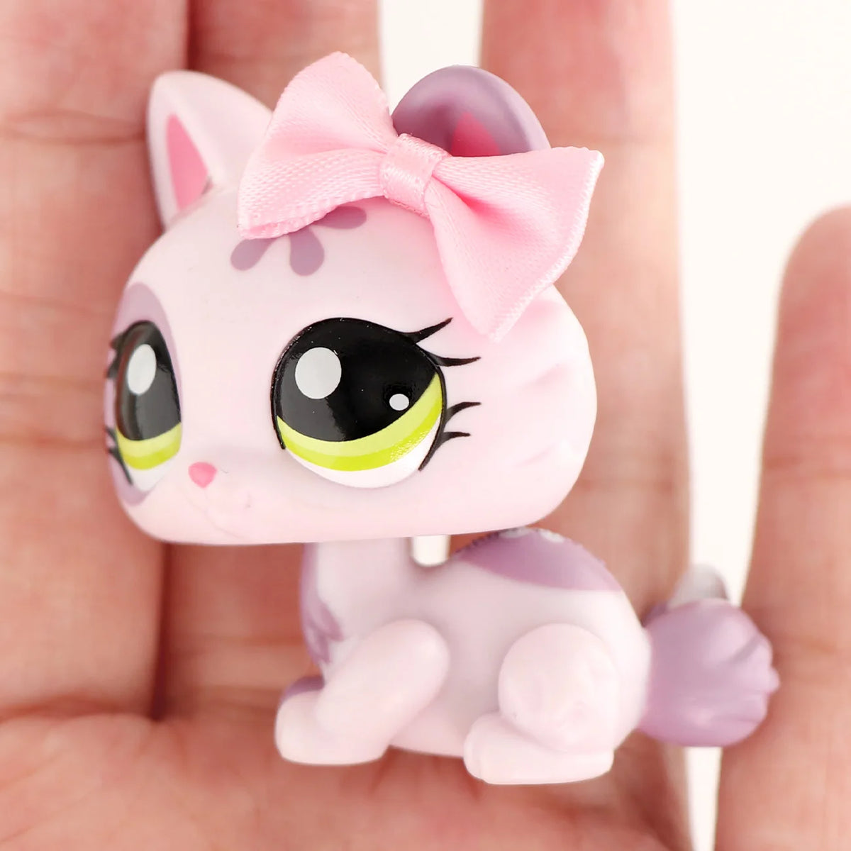A pink miniature pet animal figure with a bow is held in a person's hand.