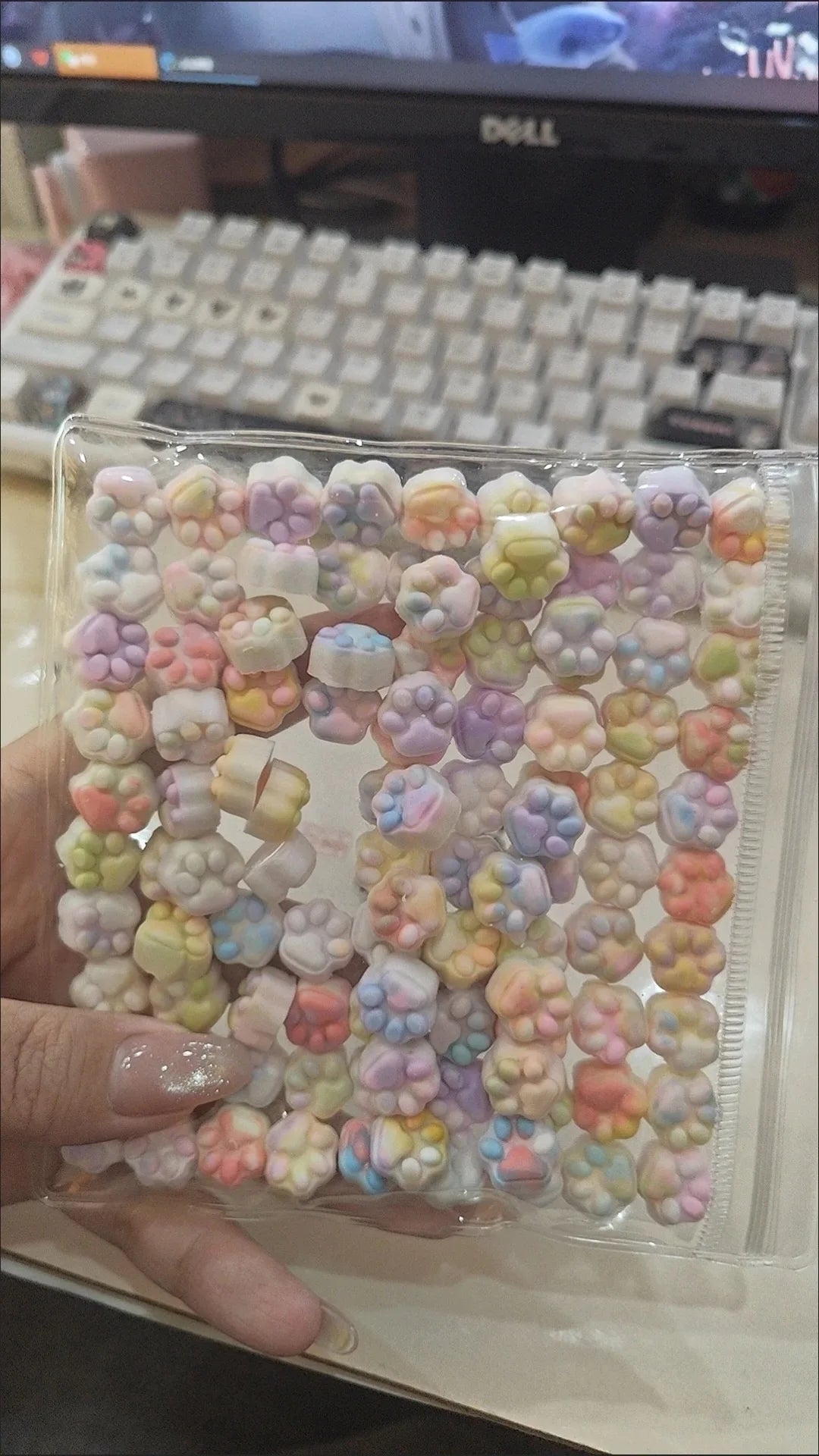 A clear plastic container filled with numerous colorful kawaii cat paw squishy stress relief fidget toys.