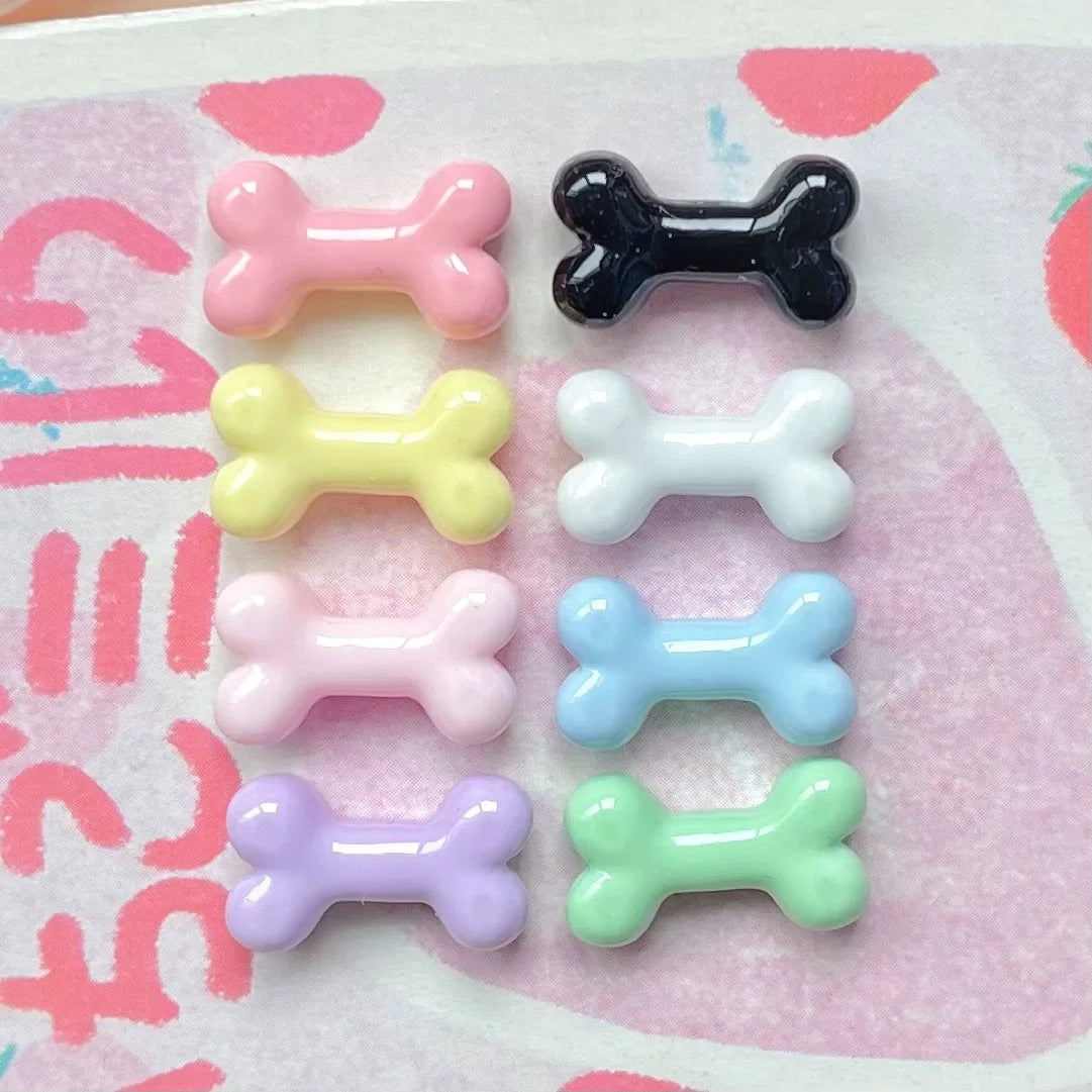A collection of six small resin bone charms in various pastel colors including pink, black, yellow, white, blue, and purple.