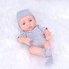 A realistic soft vinyl reborn baby doll wearing a gray knitted hat and striped outfit lies on white fluffy fabric.