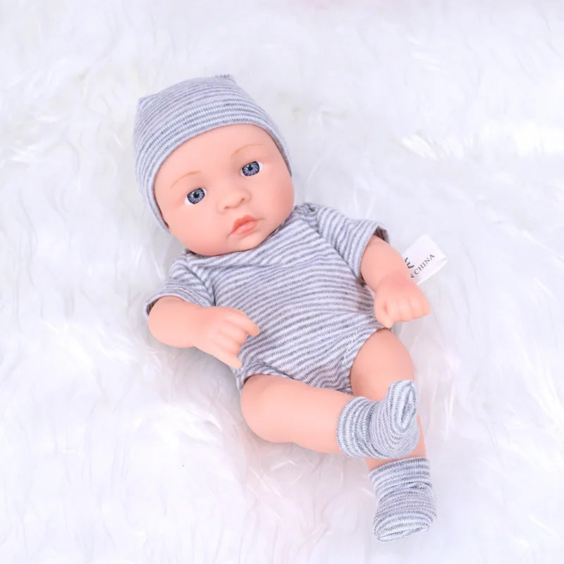A realistic soft vinyl reborn baby doll wearing a gray knitted hat and striped outfit lies on white fluffy fabric.