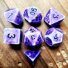 A collection of purple polyhedral dice, including d6s and d10s, resting on a wooden surface.
