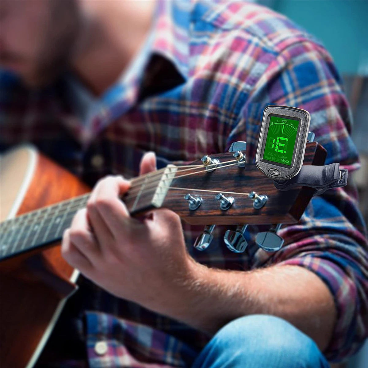 A person is using a clip-on tuner device on a guitar, holding the instrument with their right hand.