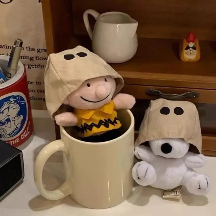 A beige plush Snoopy character is seated in a mug, with other small plush items visible on a wooden shelf.