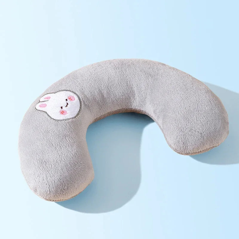 A soft gray U-shaped plush pillow with a pink face design for neck support.