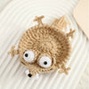 A handmade crochet lizard coaster in tan color with large eyes resting on a white surface.