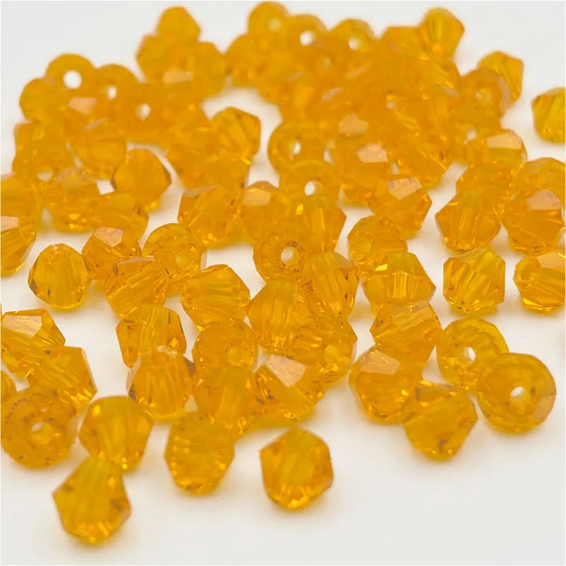 A pile of faceted, golden-yellow bicone crystal glass beads for jewelry making.