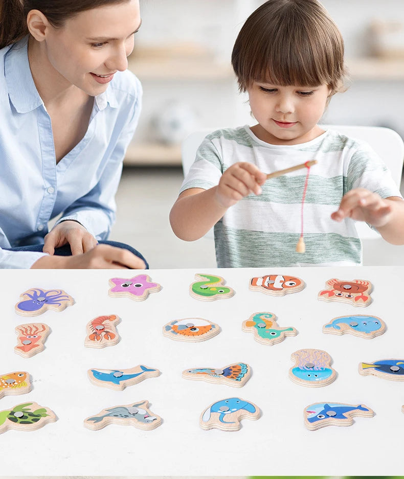 A child is playing with a set of wooden magnetic fishing game pieces on a white surface.