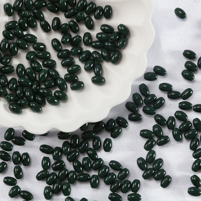 Dark green oval glass rice grain beads scattered on a white plate and fabric