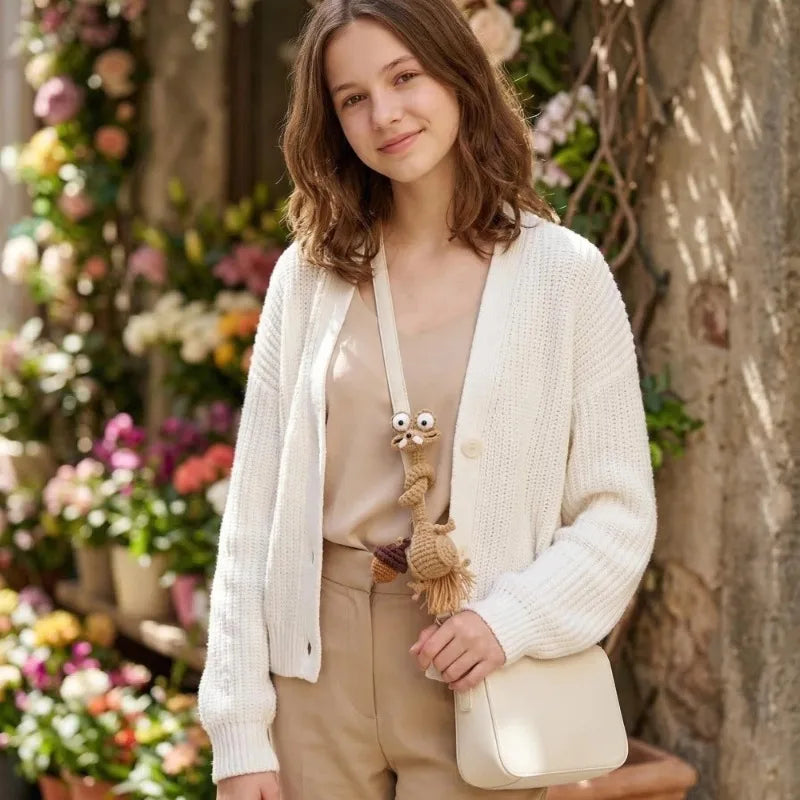 A young woman is holding a cream-colored knitted cardigan over a beige top, with a handmade crochet sloth and squirrel plush 