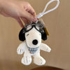 A white Snoopy plush dog with black ears and a blue plaid collar is being held by a hand, attached to a white cord.