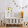 A white wooden crib with a felt forest animal mobile hanging above it against a light wall.