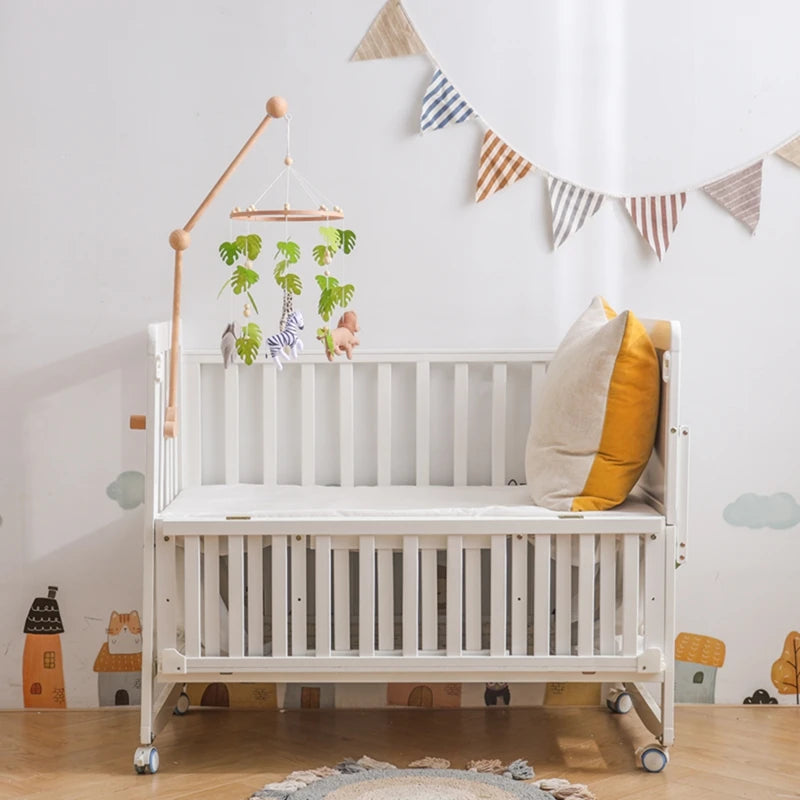A white wooden crib with a felt forest animal mobile hanging above it against a light wall.