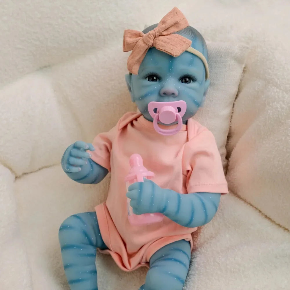 A lifelike reborn baby doll with blue skin and pink clothing sitting on a white fluffy surface.