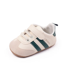 A pair of beige baby first walkers shoes with green stripes and soft soles.