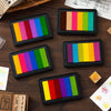 A collection of six rectangular rainbow gradient ink pads in various colors laid out on a dark wooden surface.