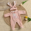 A pink bunny romper set for a baby doll lying on a woven mat with yellow flowers.