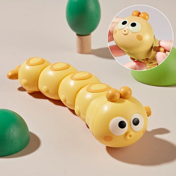 A yellow cartoon clockwork caterpillar wind up toy with large eyes and small ears is shown next to a green object.