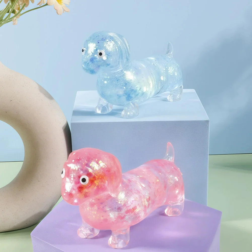 A small, squishy toy shaped like a dachshund in pink and blue translucent material resting on a purple box.