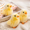 A close-up of three adorable yellow chick plush toys resting on a white knitted fabric.