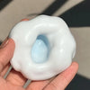 A hand holds a white, squishy stress relief ball with a blue center.