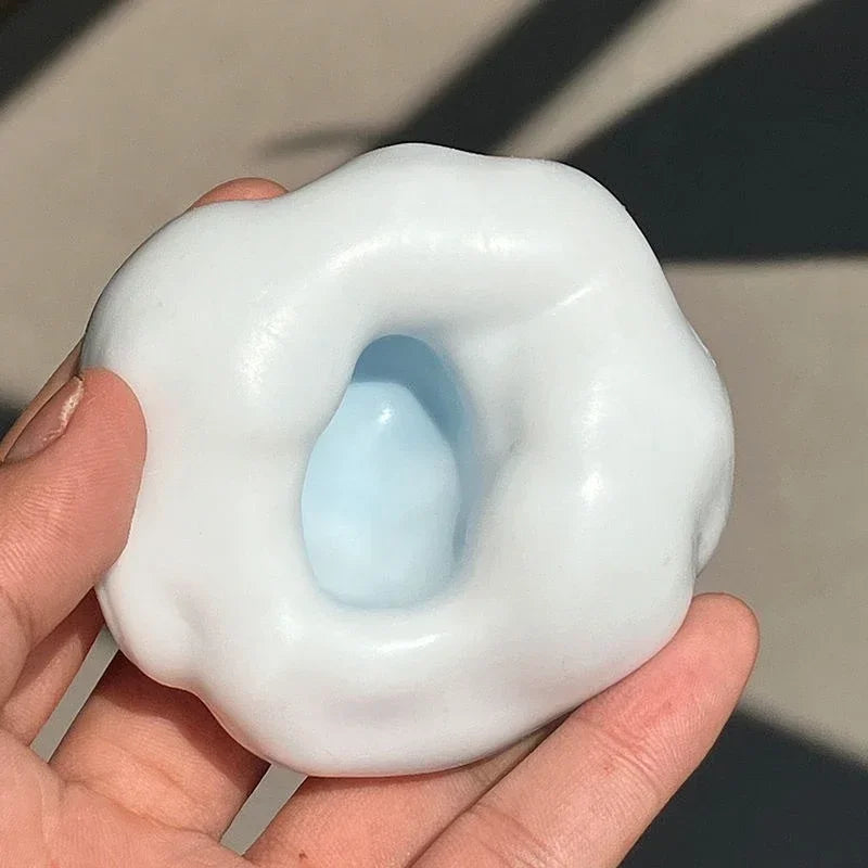 A hand holds a white, squishy stress relief ball with a blue center.