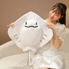 A woman holds a white plush toy shaped like a ray fish with black features against a light background.