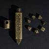 A brass bullet box with a threaded top and a circular arrangement of small metal dice on a dark surface.