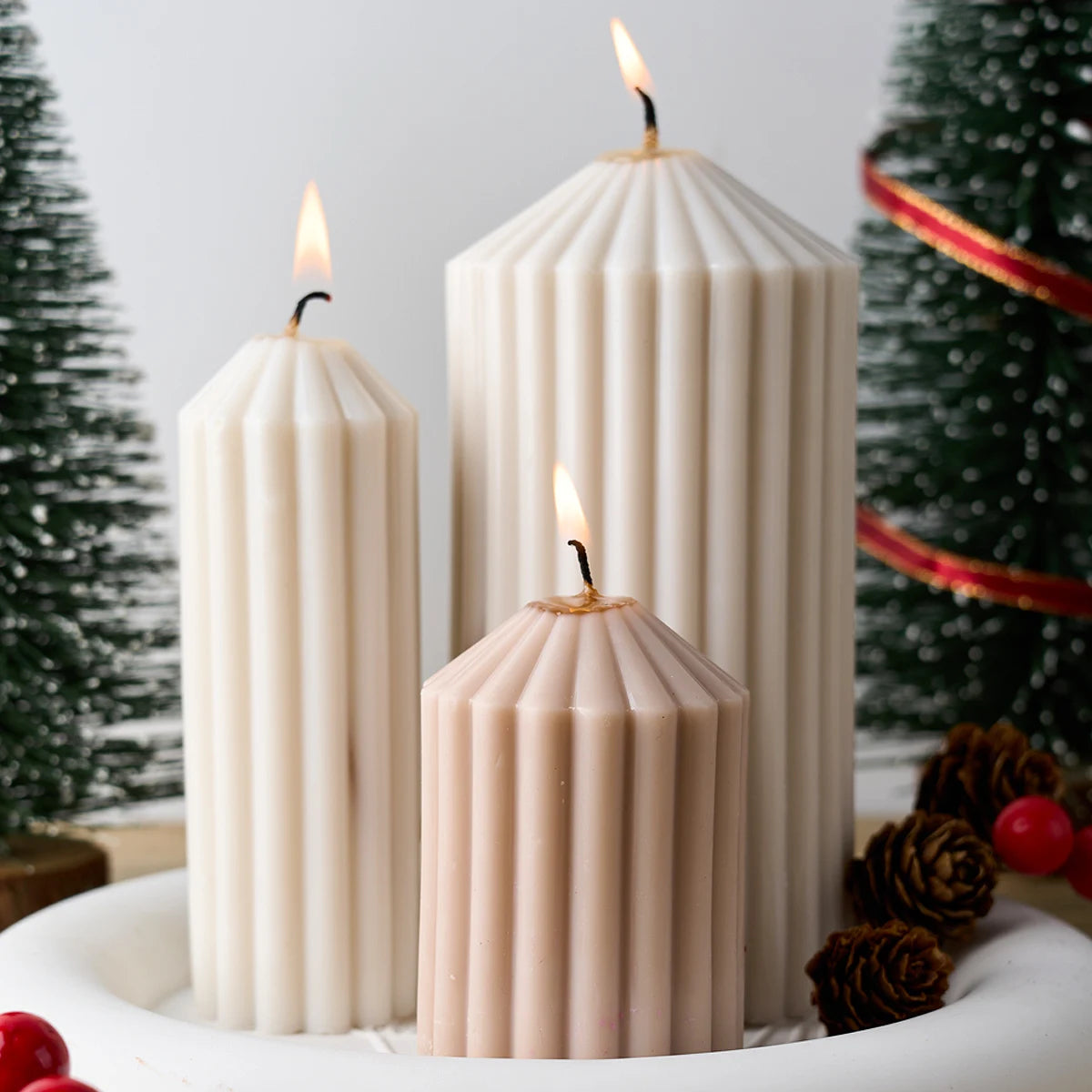 A grouping of three white candles in varying heights with lit flames on a white surface.