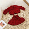 A deep red knitted outfit set for a baby doll displayed on a woven mat.