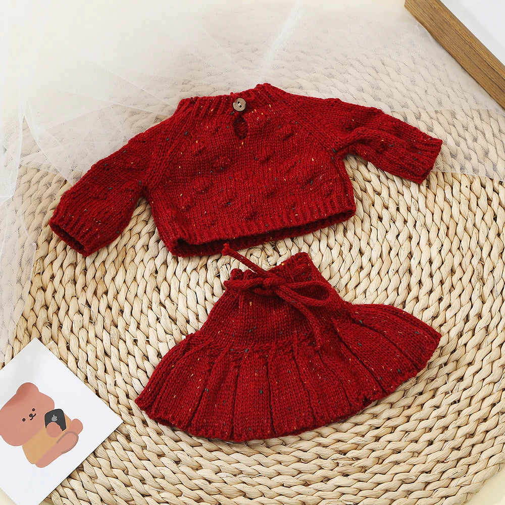 A deep red knitted outfit set for a baby doll displayed on a woven mat.
